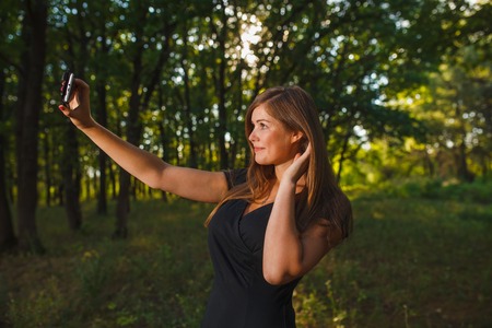 girl woman sELF making self photo on the phone on nature green background summer forestの写真素材