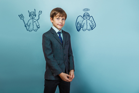 a boy of twelve European appearance in a suit holding a blank sheet on a  gray  backgroundの写真素材