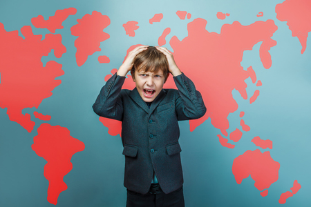 a boy of twelve European appearance in a suit holding a blank sheet on a  gray  backgroundの写真素材
