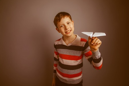 boy teenager European appearance Brown launches a paper airplane white hand on a gray background, fun, game retroの写真素材
