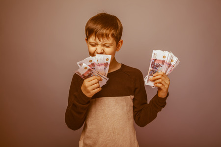 baby boy teenager European appearance holds a brown hair bill and laughs on gray background, happiness, wealth retroの写真素材