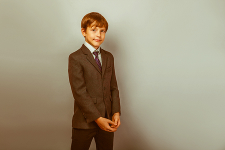 a boy of twelve European appearance in a suit is smiling portrait on a gray background retroの写真素材