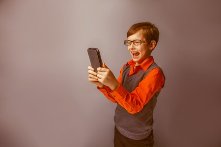European-looking boy  of ten  years in  glasses  holding tablet in hand, plays  on a blue background retroの写真素材