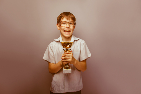 a boy of 10 years of European appearance with glasses holding a cup in his hands on a gray background retroの写真素材