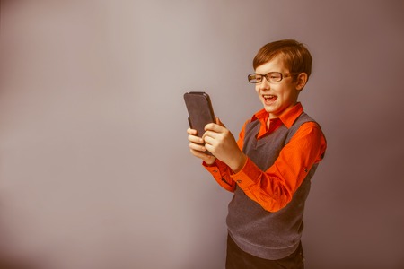 European-looking  boy of ten years  in  glasses holding tablet in hand, plays, pleasure on a blue background retroの写真素材