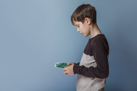 Boy teenager European appearance ten years counting money on a gray backgroundの写真素材