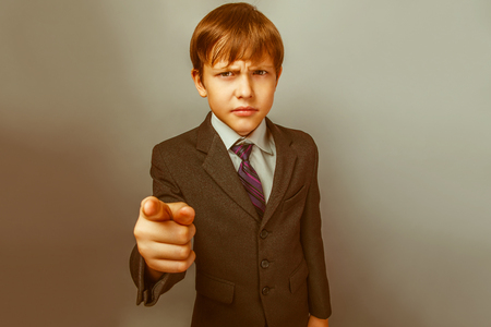 a boy of twelve European appearance in a suit shows a finger at the camera on a gray background retroの写真素材