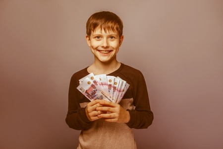 Boy teenager European appearance ten years holding a wad of money on a gray  background retroの写真素材