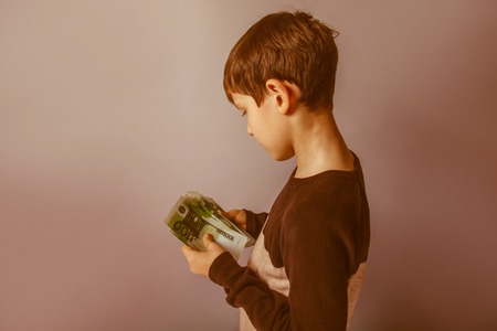Boy teenager ten years  European appearance holding a wad  of money on a gray  background retroの写真素材