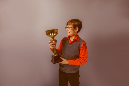 European-looking  boy of ten years in glasses holding a cup award on a blue background retroの写真素材
