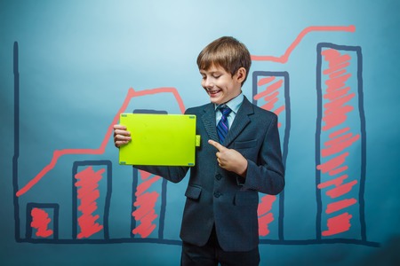 a boy of twelve European appearance in a suit holding a blank sheet on a  gray  backgroundの写真素材