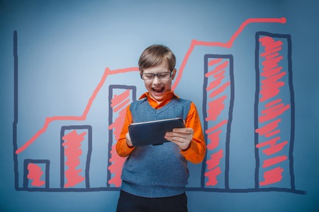 a boy of twelve European appearance in a suit holding a blank sheet on a  gray  backgroundの写真素材