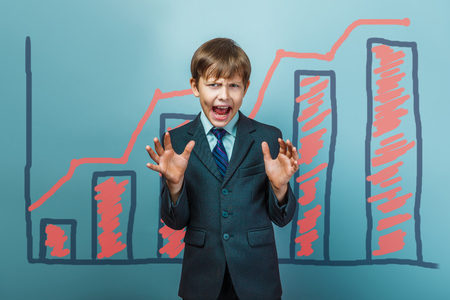 a boy of twelve European appearance in a suit holding a blank sheet on a  gray  backgroundの写真素材
