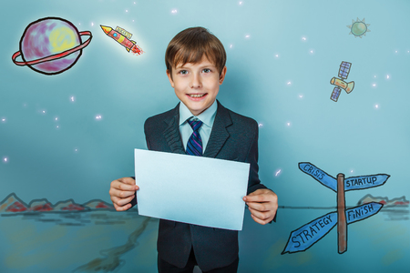 a boy of twelve European appearance in a suit holding a blank sheet on a  gray  backgroundの写真素材