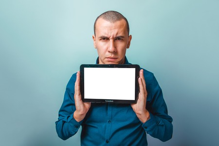 a man of European appearance thirty years, holding a tablet frowns on a gray backgroundの写真素材