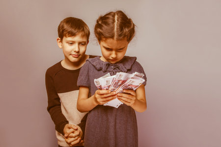 teenage boy and girl  holding  money bills in his  hands on a  gray  background retroの写真素材