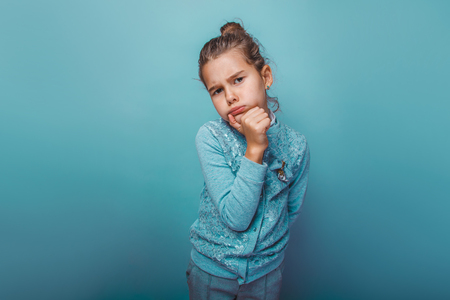 teen girl of European appearance seven years thinking pouted holds his hand to his chin on a gray  backgroundの写真素材