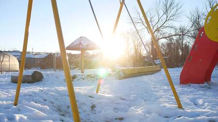 swing for children swinging on playground sun glare snow winterの写真素材