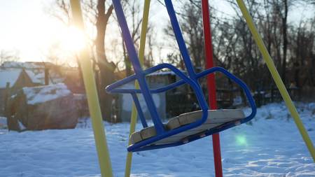 swing for children swinging on playground snow winter sun glareの写真素材