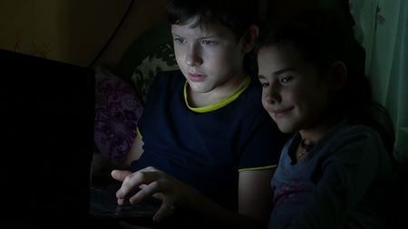 children boy and girl playing in the laptop at night online gameの写真素材