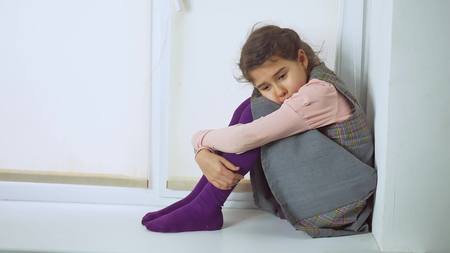sad young teen girl sitting by the window, looking out the windowの写真素材