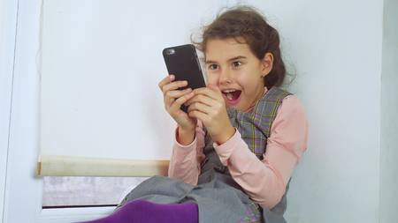 teen girl sitting on a window sill web plays the online game for smartphoneの写真素材
