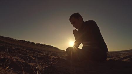 Man praying at sunset god sitting silhouette sun sunlight the religionの写真素材