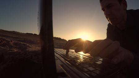 man laptop. businessman freelancer silhouette man laptop working behind sitting on beach freelancing in the sunの写真素材