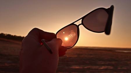 travel. Hand holds sunglasses at sunset lifestyle natureの写真素材