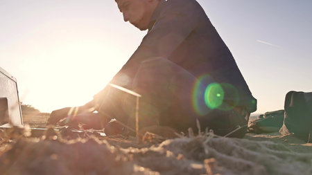 Freelancer. Man silhouette working on laptop freelancer sitting on the sand sunset sun glare sun