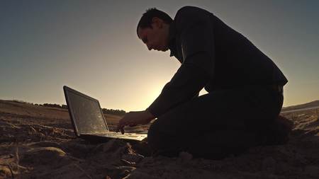 man businessman laptop freelancer working behind sitting on beach freelancing silhouette in the sunの写真素材