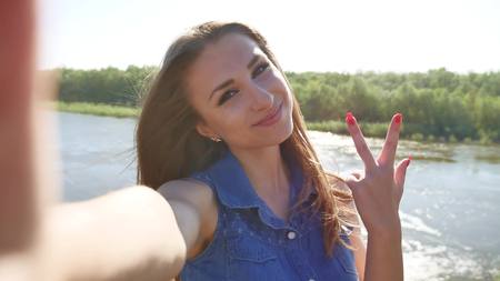 Girl doing selfie on nature on smartphone. The girl lifestyle takes pictures of herselfの写真素材