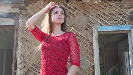 Beautiful girl lifestyle in a red dress. Sexy girl in a dress is standing next to the old house of the ruinsの写真素材