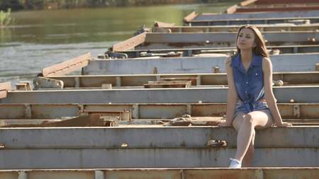 The girl is sitting on the bridge. Sexy beautiful girl lifestyle sits on the bridge outdoorの写真素材