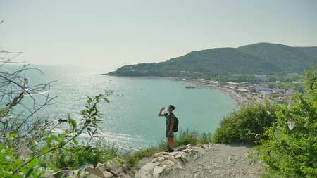 Boy teenager tourist travels through the mountains by the sea. Boy traveler drinks water thirstyの写真素材