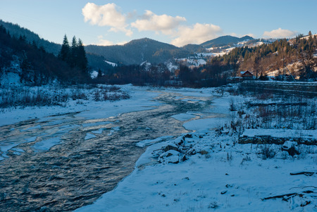 Winter Carpathian mountains landscape with ice covered river near villageの写真素材