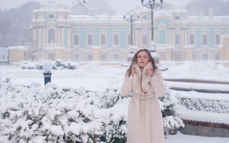 Winter portrait of a woman in white coat during snowfall in a parkの写真素材