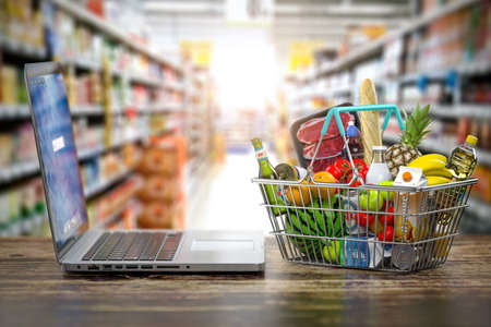 Grocery food buying online and delivery concept. Shopping basket full of food and laptop on the shelf of supermarket. 3d illustrationの写真素材