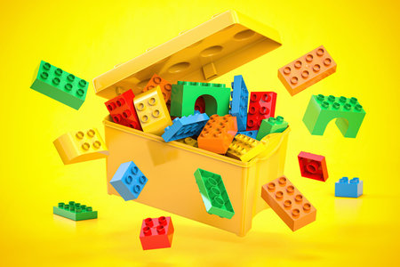 Box full of colorful toy plastic bricks and blocks on yellow background. Delivery children gifts and...