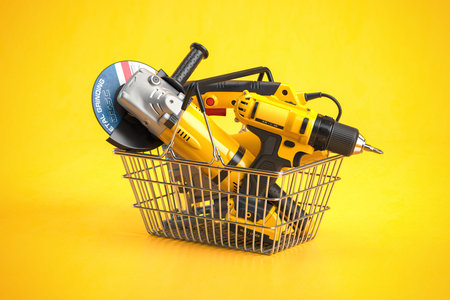 Shopping basket with electric tools and construction equipment angle grinder, electric drill and jigsaw on yellow. Selling and buying online. 3d illustrationの写真素材