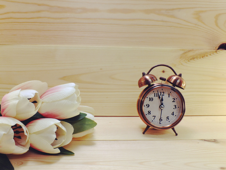 alarm clock and white flowers in pink vase on brown wood tableの写真素材