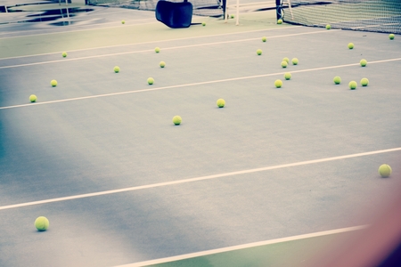 ground court with net and many yellow tennis ballsの写真素材
