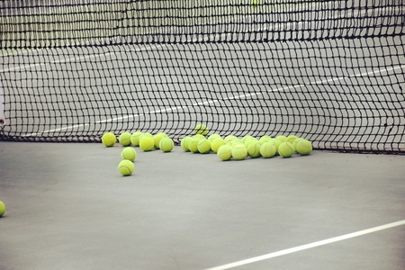 ground court with net and many yellow tennis ballsの写真素材