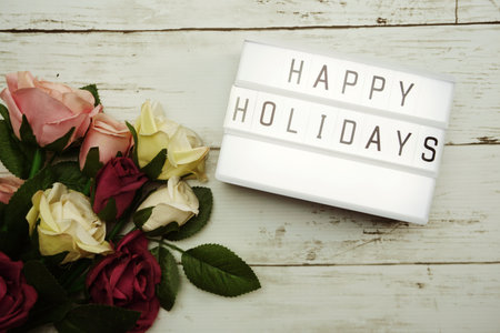 Happy Holidays Word on Light box with roses flower bouquet on wooden background
