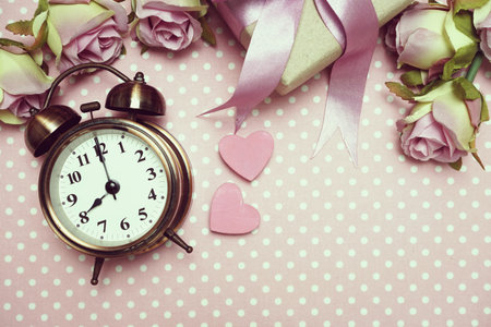 Alarm clock and gift box with roses bouquet with space copy on pink polka dot background