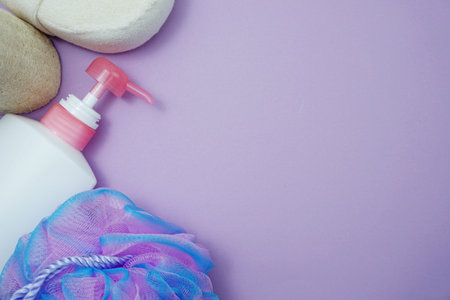 Flat lay bath products shower bottle with shower puff and sponge on purple background