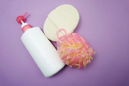 Flat lay bath products shower bottle with shower puff and sponge on purple background