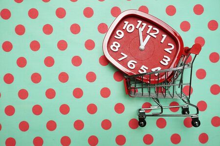 Red Alarm clock and Trolley Mini Shopping Cart on green polka dot backgroundの写真素材