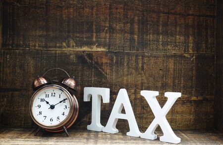 time to pay tax concept tax alphabet letters and alarm clock on wooden backgroundの写真素材