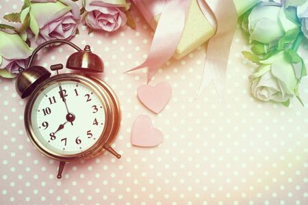 Alarm clock and gift box with roses bouquet with space copy on pink polka dot backgroundの写真素材